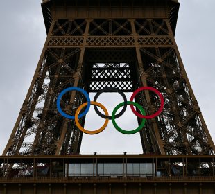A photo of the Eiffel tower during the 2024 Paris Games. The tower has the 5 Olympic rings logo hung from it.