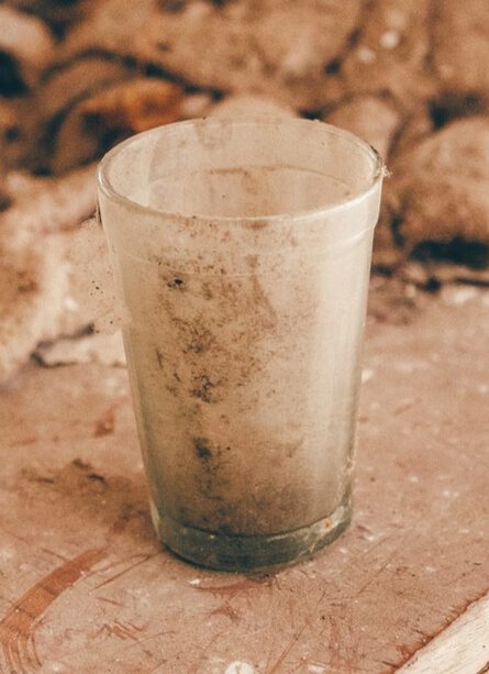 A dirty glass sits on a dusty countertop
