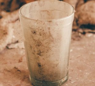 A dirty glass sits on a dusty countertop