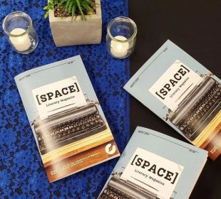 Three [SPACE] magazines laid on a table. A blue lace tablecloth, decorative plant, and two candles are also on the table.