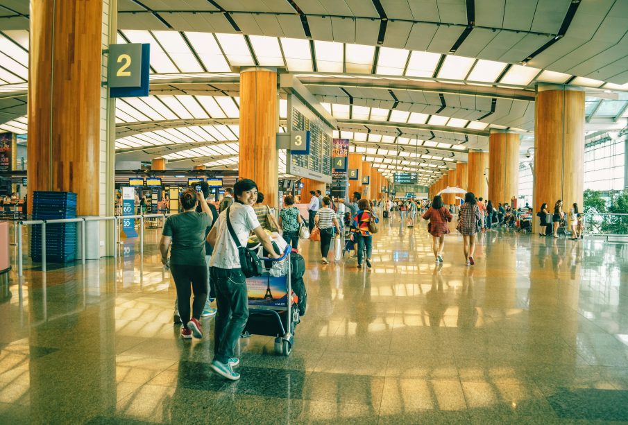 A smiling youth at an airport, with a trolley of luggage.