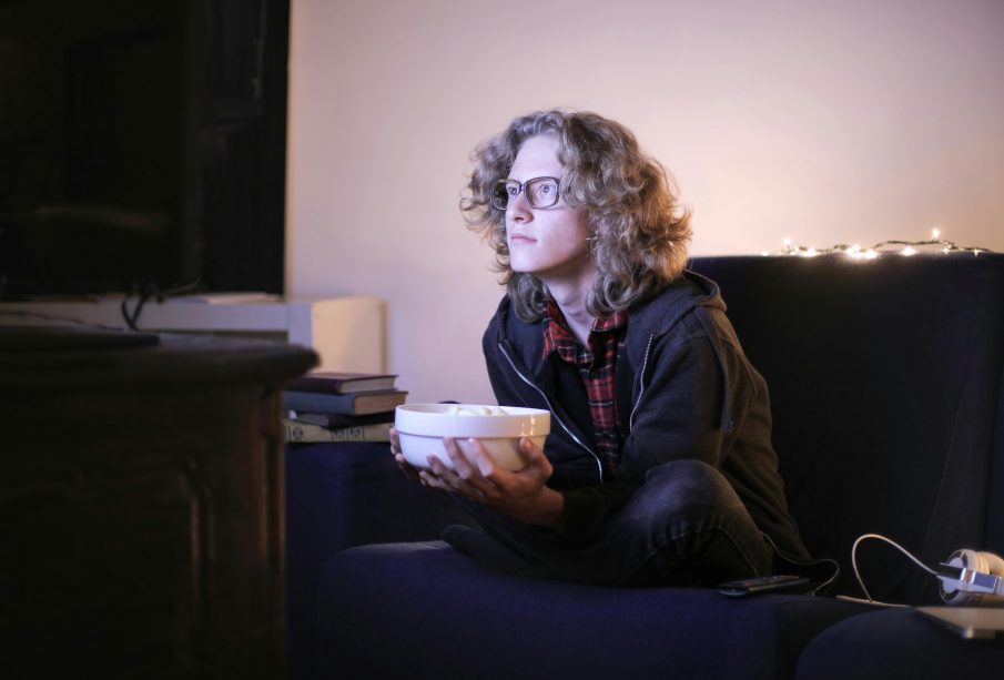 A photo of a person sitting on a couch, with a bowl of snacks, intently watching TV.