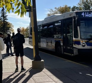 A photo of a bus standing at a stop, some people waiting to get on.