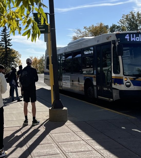 A photo of a bus standing at a stop, some people waiting to get on.
