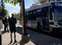 A photo of a bus standing at a stop, some people waiting to get on.