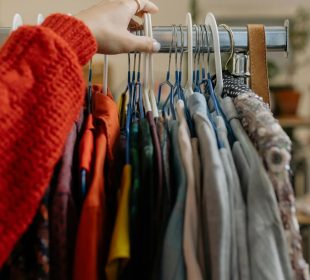 An arm in a red sleeve reaching for a piece of clothing among a rack of various clothing items.