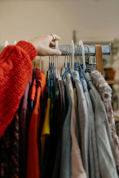 An arm in a red sleeve reaching for a piece of clothing among a rack of various clothing items.