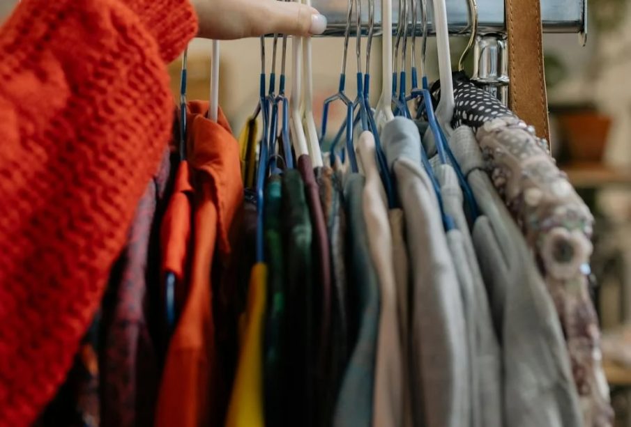 An arm in a red sleeve reaching for a piece of clothing among a rack of various clothing items.