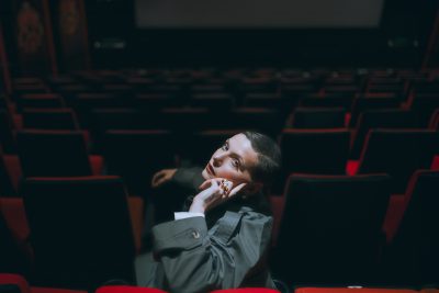 A photo of the artist Elena Erin, sitting, looking at the camera.