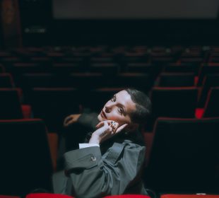 A photo of the artist Elena Erin, sitting, looking at the camera.
