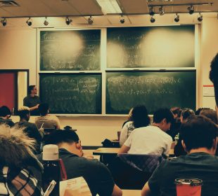 A photo of a classroom from the back of the class, the blackboard is filled with math.