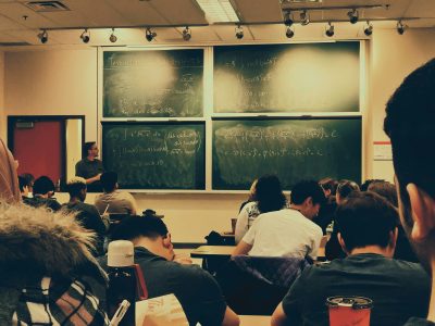 A photo of a classroom from the back of the class, the blackboard is filled with math.