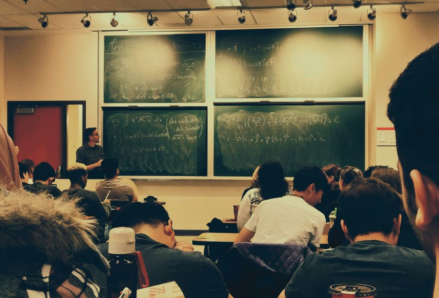 A photo of a classroom from the back of the class, the blackboard is filled with math.