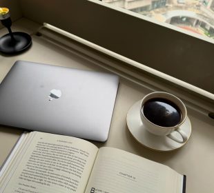 A photo showing a cup of coffee, an open book and a laptop.