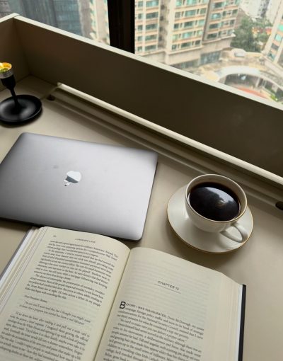 A photo showing a cup of coffee, an open book and a laptop.