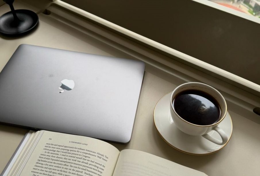 A photo showing a cup of coffee, an open book and a laptop.