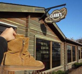 A pair of boots being held up next to the sign of a repair shop named Clark’s.