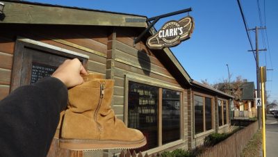 A pair of boots being held up next to the sign of a repair shop named Clark’s.