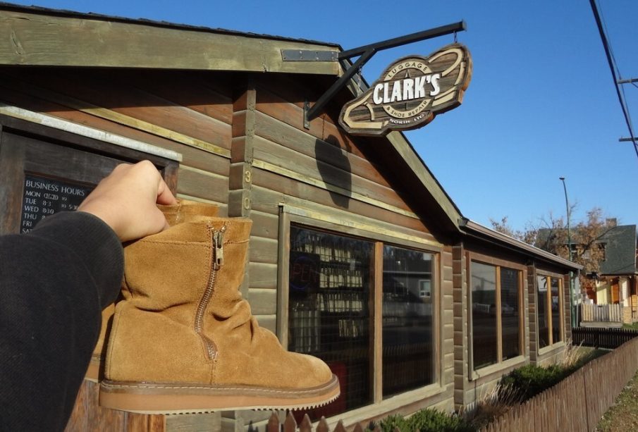 A pair of boots being held up next to the sign of a repair shop named Clark’s.