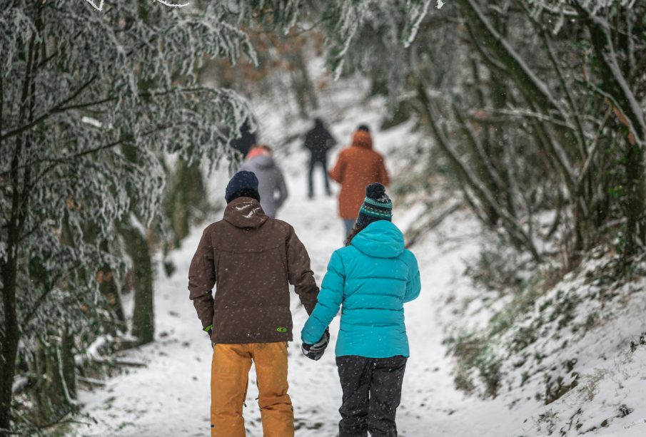 A couple in winter gear walking down in a path in snowy woods, more people ahead.