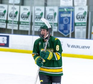 Jules Stokes on the ice with her hockey stick, helmet and Cougars jersey, smiling.