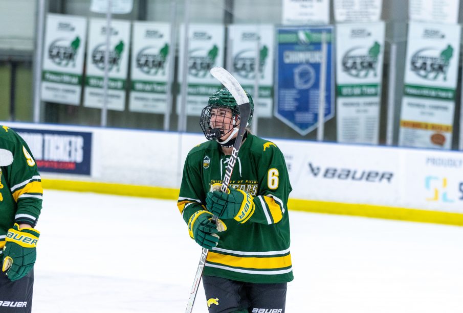 Jules Stokes on the ice with her hockey stick, helmet and Cougars jersey, smiling.