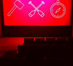 A blank movie theatre screen lit only by red lights shows lineart symbols of an axe, crossed canoe paddles, and a compass in white