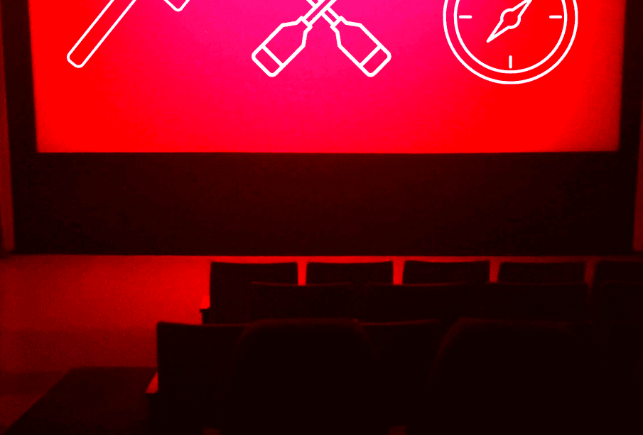 A blank movie theatre screen lit only by red lights shows lineart symbols of an axe, crossed canoe paddles, and a compass in white