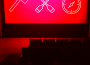 A blank movie theatre screen lit only by red lights shows lineart symbols of an axe, crossed canoe paddles, and a compass in white