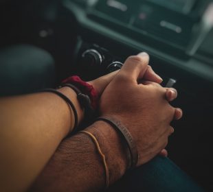 Close up of two individuals holding hands in a car with a blurred stereo in the background