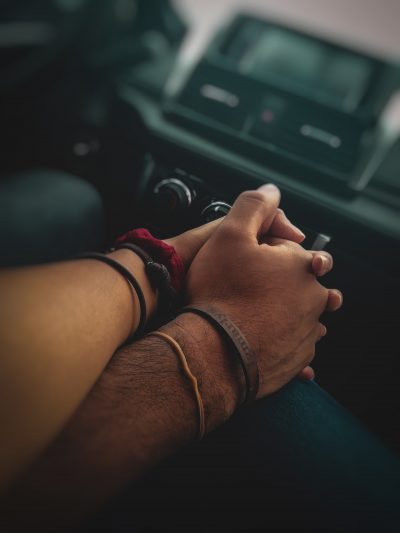 Close up of two individuals holding hands in a car with a blurred stereo in the background