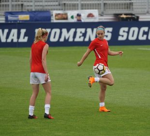 Two women practice soccer on a grass field