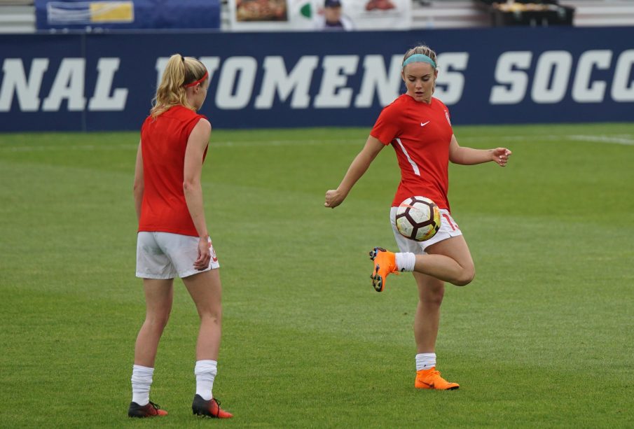 Two women practice soccer on a grass field