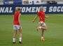 Two women practice soccer on a grass field
