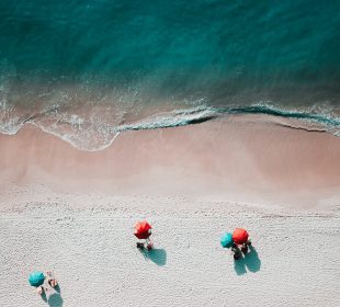 Above view of a beach with umbrellas and a few patrons around the edge of the water