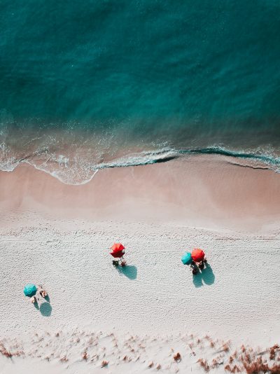 Above view of a beach with umbrellas and a few patrons around the edge of the water