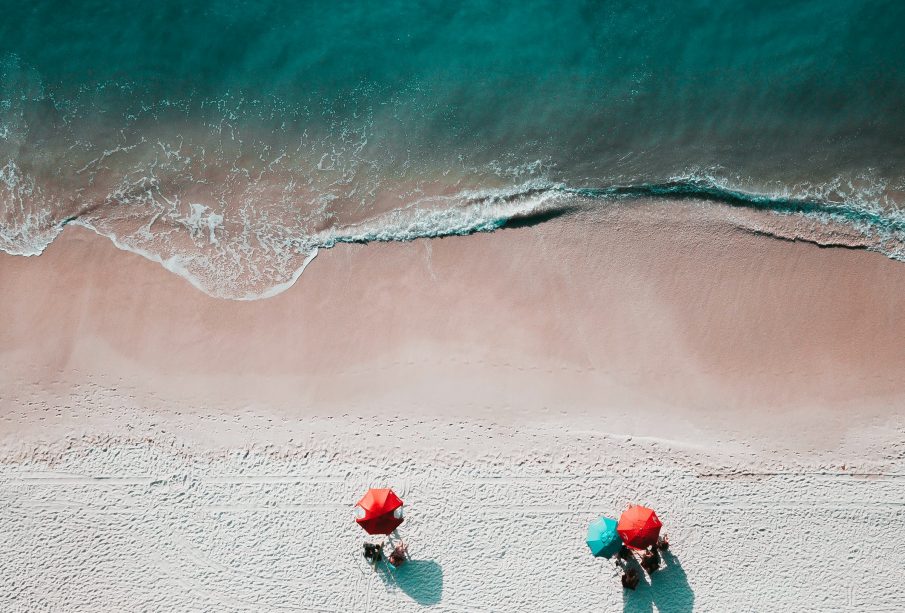 Above view of a beach with umbrellas and a few patrons around the edge of the water