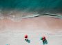Above view of a beach with umbrellas and a few patrons around the edge of the water