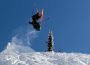 A skier jumps off a ramp, doing a flip mid-air with the orange bottoms of their skis in full view.
