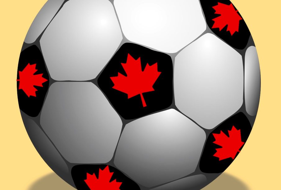 A soccer ball sits against a yellow background, and every black patch on the soccer ball has a red maple leaf in the middle of the patch.