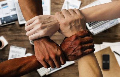 This is a photo of four arms of varying skin tones holding onto each other. Each hand is clutching a wrist, creating a perfect square, or an endless connection.