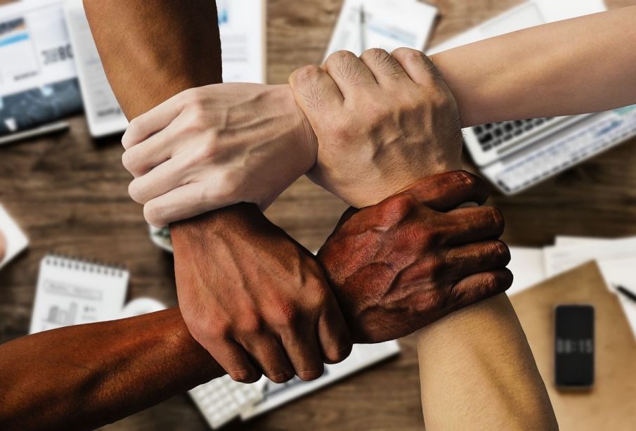 This is a photo of four arms of varying skin tones holding onto each other. Each hand is clutching a wrist, creating a perfect square, or an endless connection.