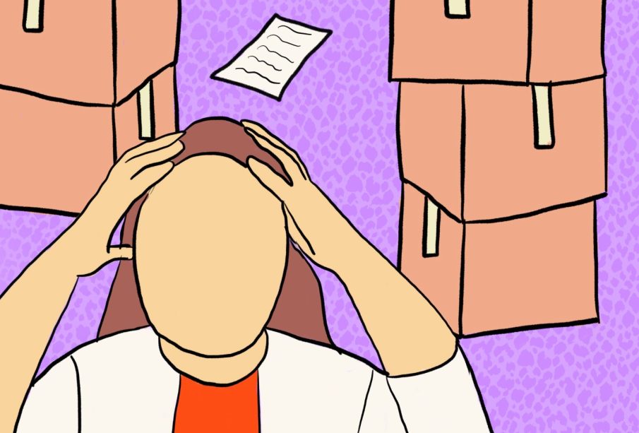 A person with both hands on their head, with some papers strewn around the floor and boxes in the background.