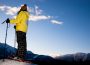 A person stands on a mountain top in their snowshoes, taking in the scenic view.