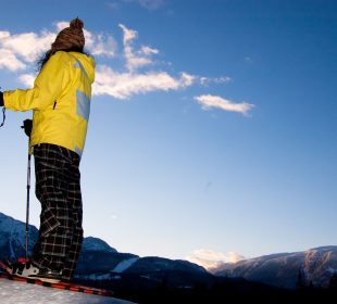 A person stands on a mountain top in their snowshoes, taking in the scenic view.
