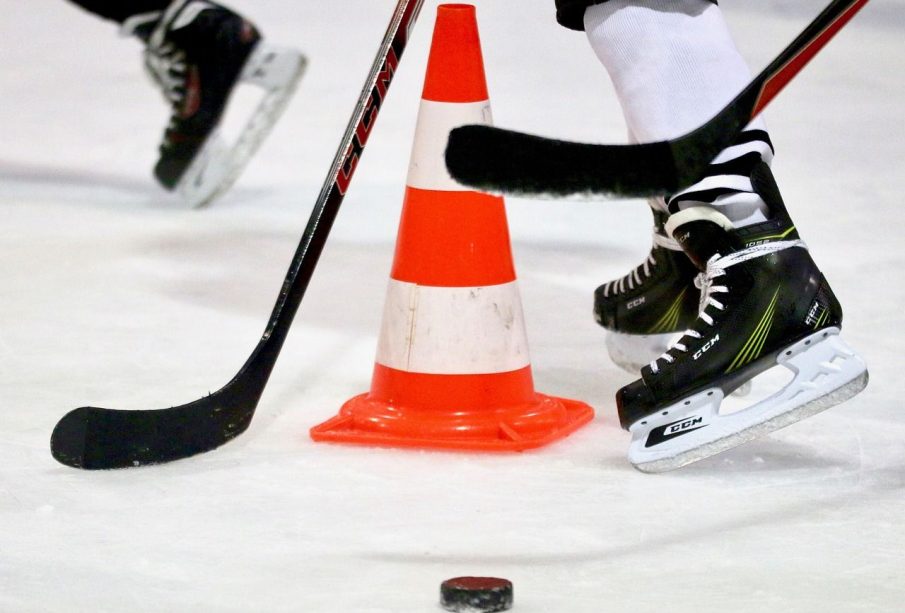 A few hockey players skate around a puck and safety cone on the ice.