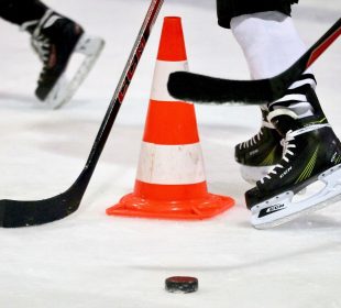 A few hockey players skate around a puck and safety cone on the ice.