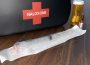 A black naloxone kit sits on a wooden table, with a still-packaged needle and three vials of the liquid injection sit beside it.