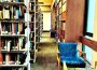 A photo looking down an aisle in Campion Library, showing shelves of books along each side and chairs beside windows to the right.