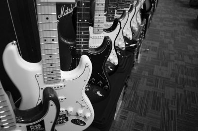 Several electric guitars sit lined up in a row on display with an amplifier in the background.